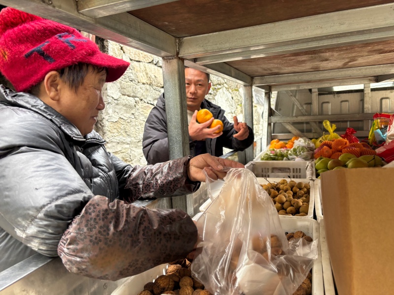 周刚（后）正在给村民卖货的同时给村民赠送橘子.jpg